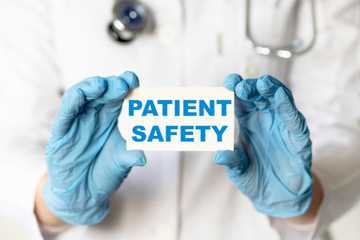 A medical worker in gloves holds a card with the words patient safety medical concept