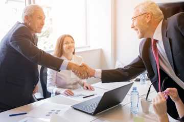 smiling-woman-looking-two-senior-businessman-shaking-hands